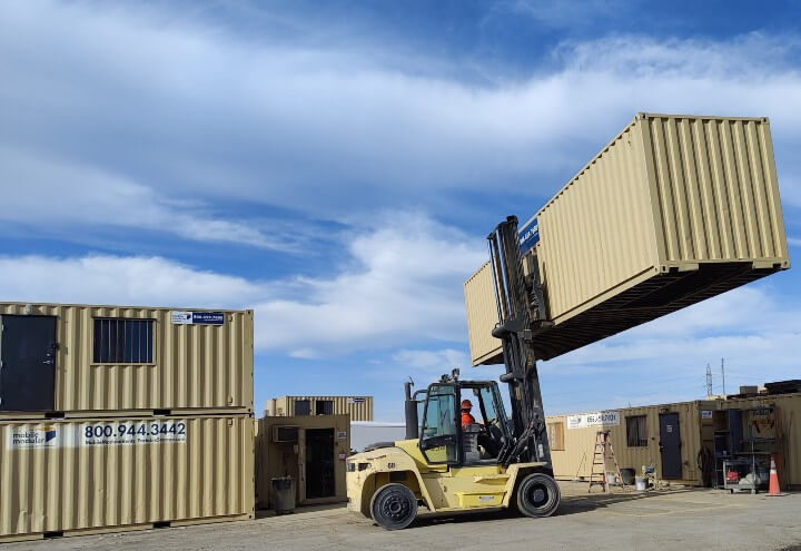man operating forklift with portable shipping container lifted in the air