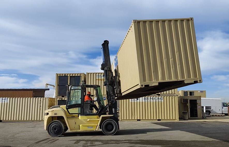 man operating a forklift with a large shipping container in midair